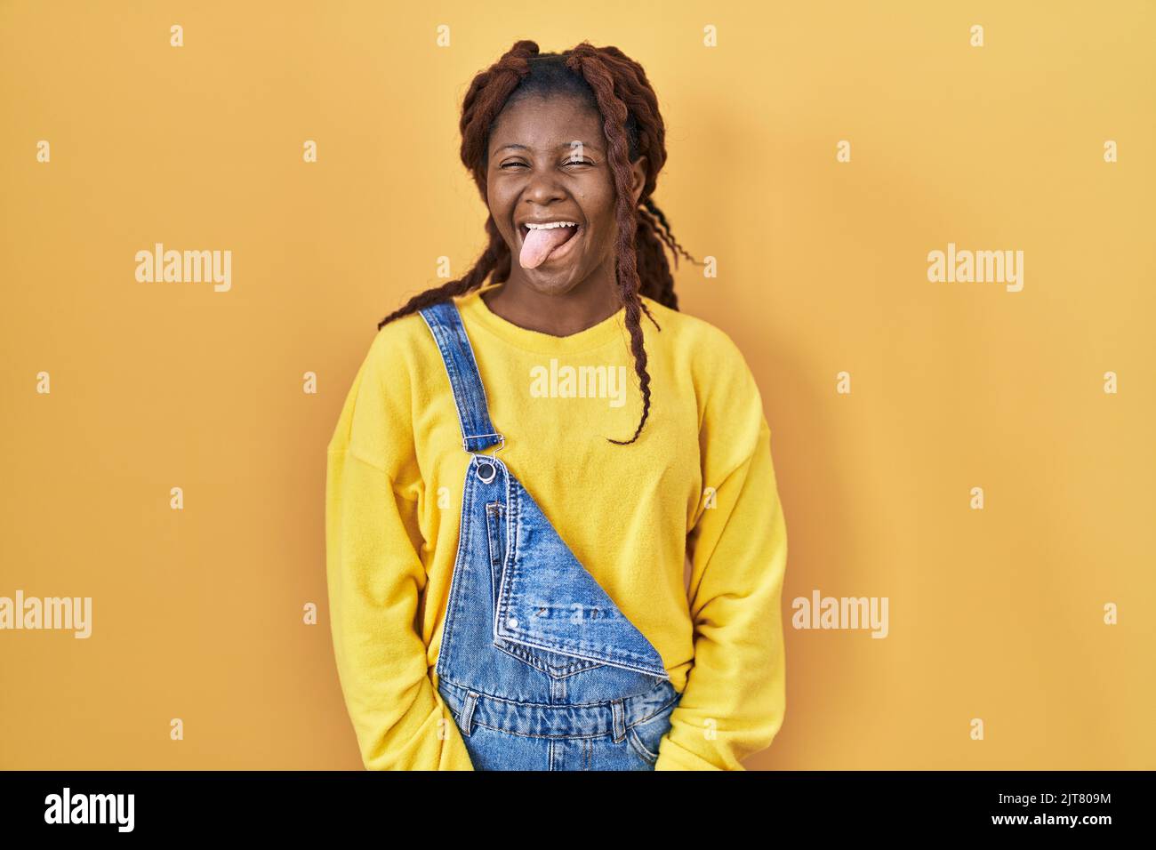 African woman standing over yellow background sticking tongue out happy ...