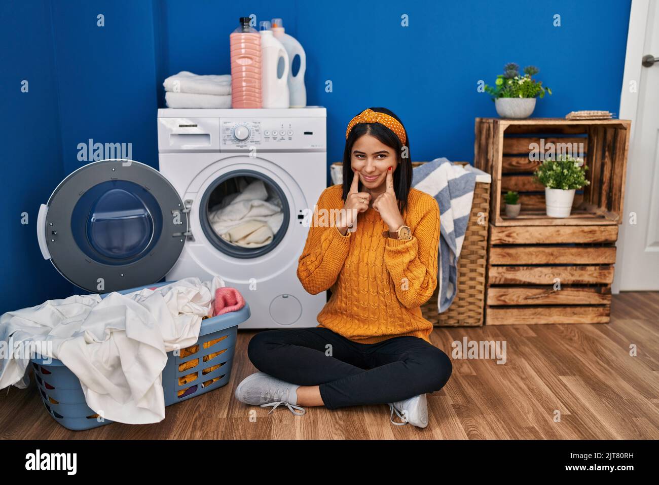 Young hispanic woman doing laundry smiling with open mouth, fingers
