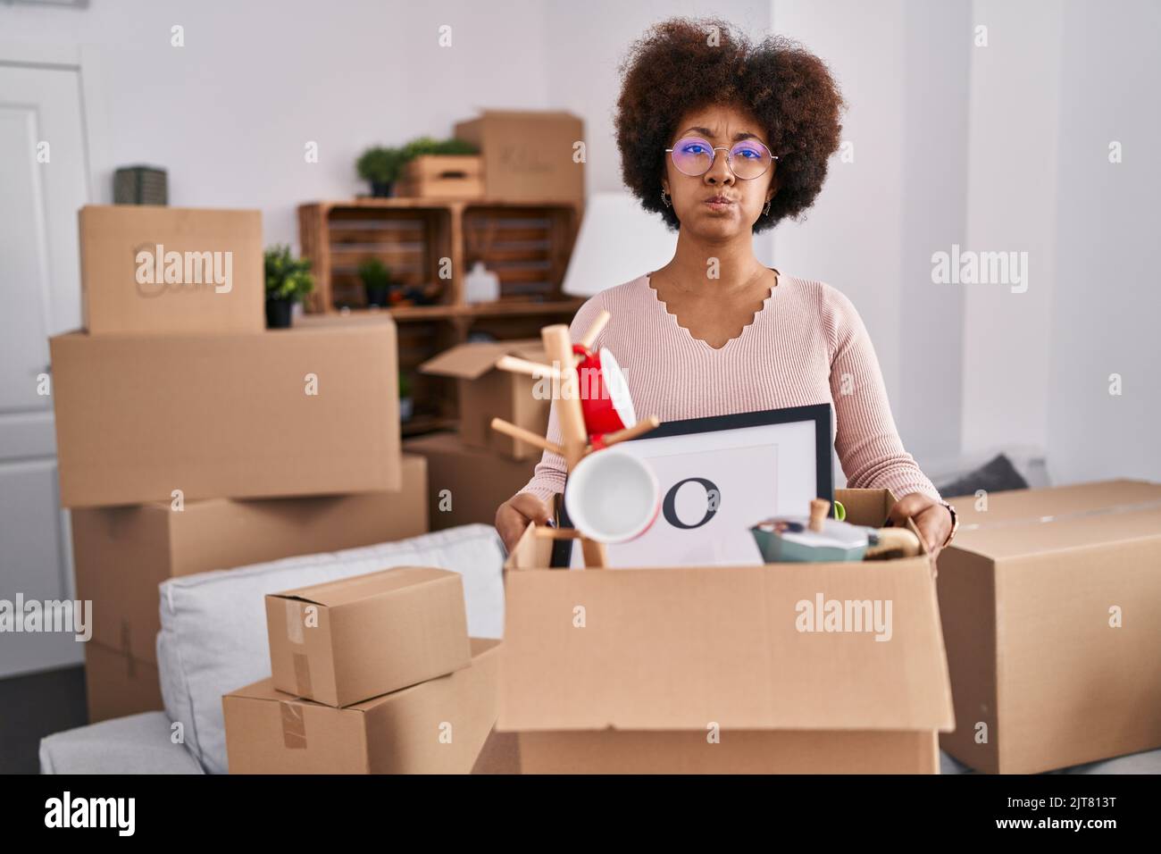 Young african american woman moving to a new home puffing cheeks with ...