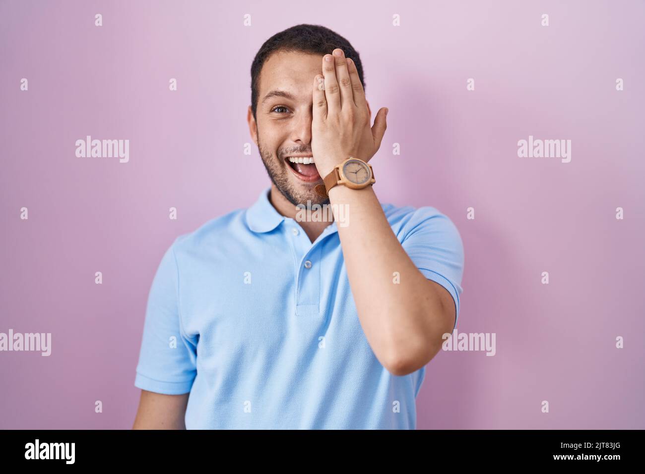 Hispanic man standing over pink background covering one eye with hand ...