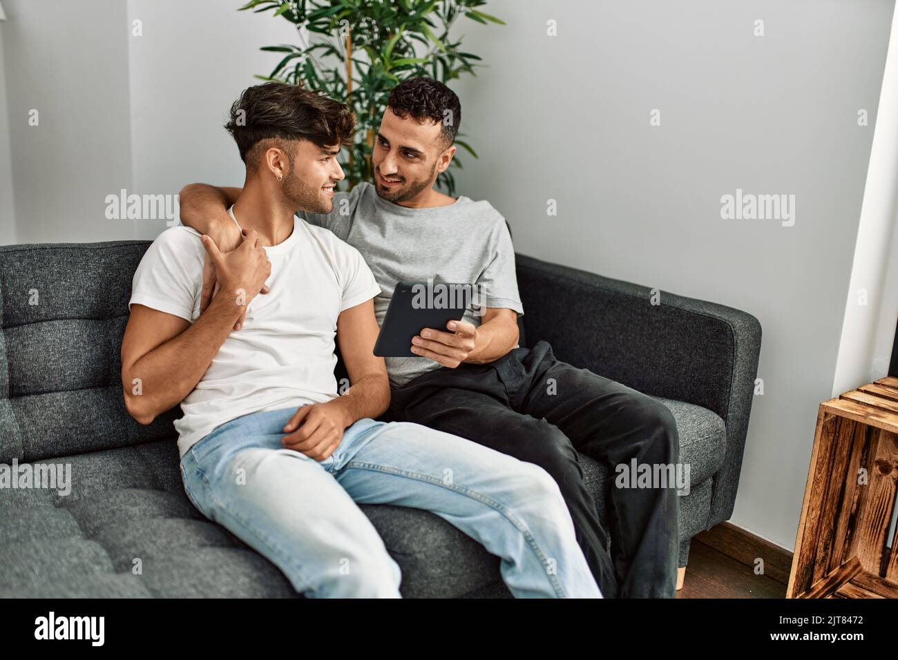 Two hispanic men couple using touchpad hugging each other at home Stock ...