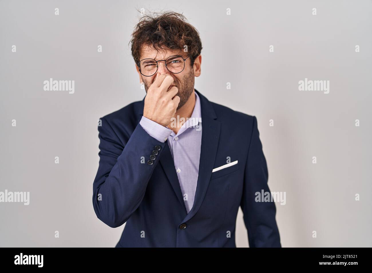 Hispanic business man wearing glasses smelling something stinky and