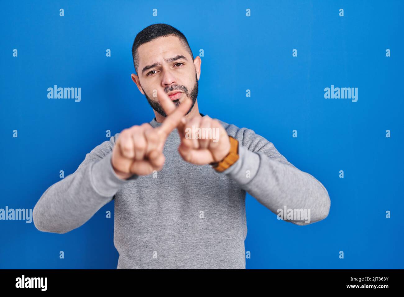 Hispanic man standing over blue background rejection expression ...