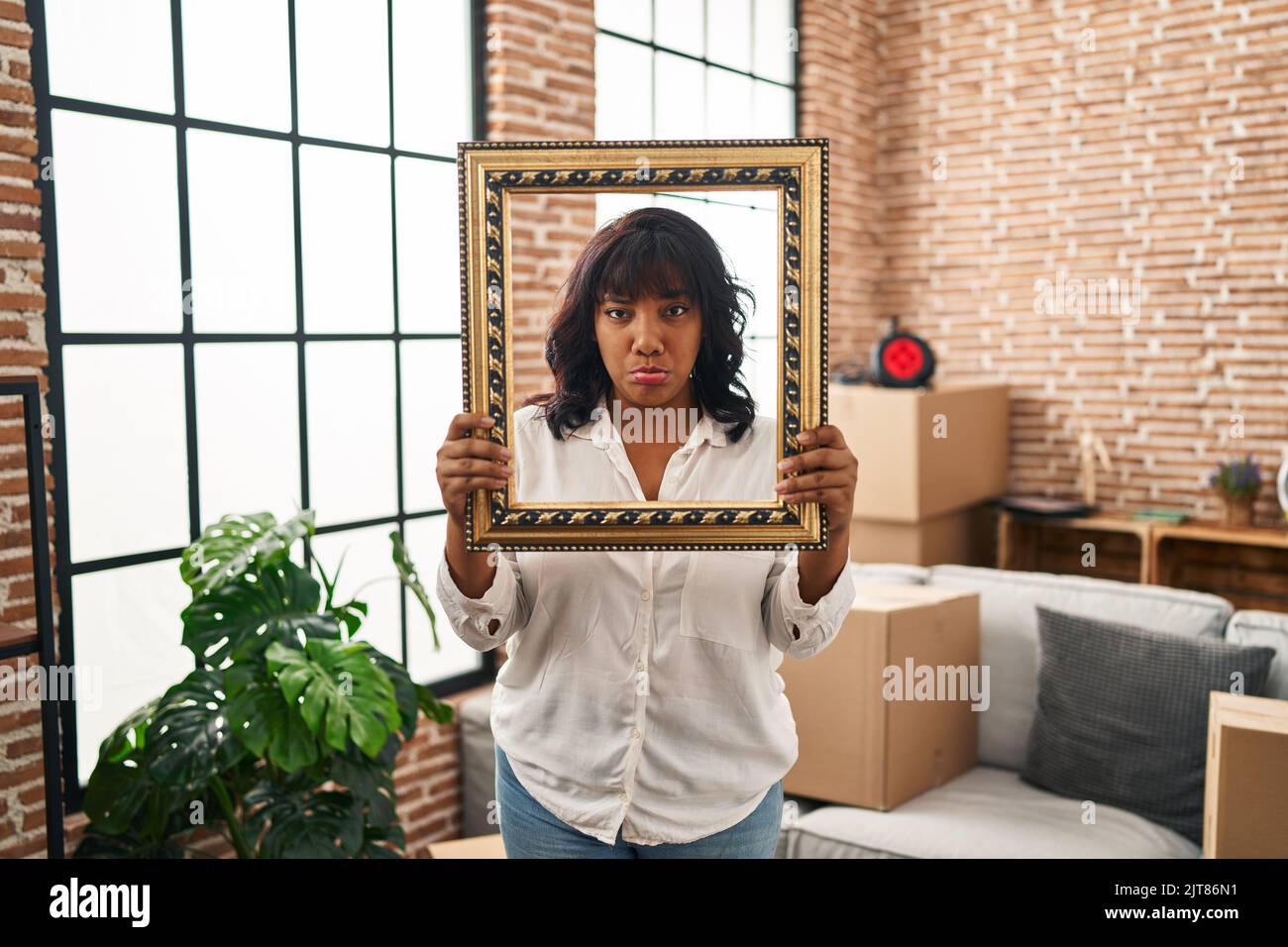 Hispanic woman at new home holding empty frame depressed and worry for ...