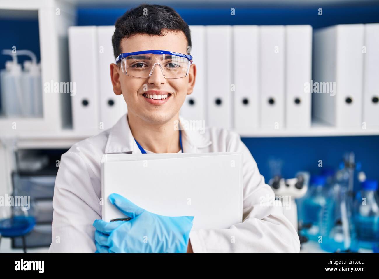 Young non binary man scientist smiling confident hugging binder at