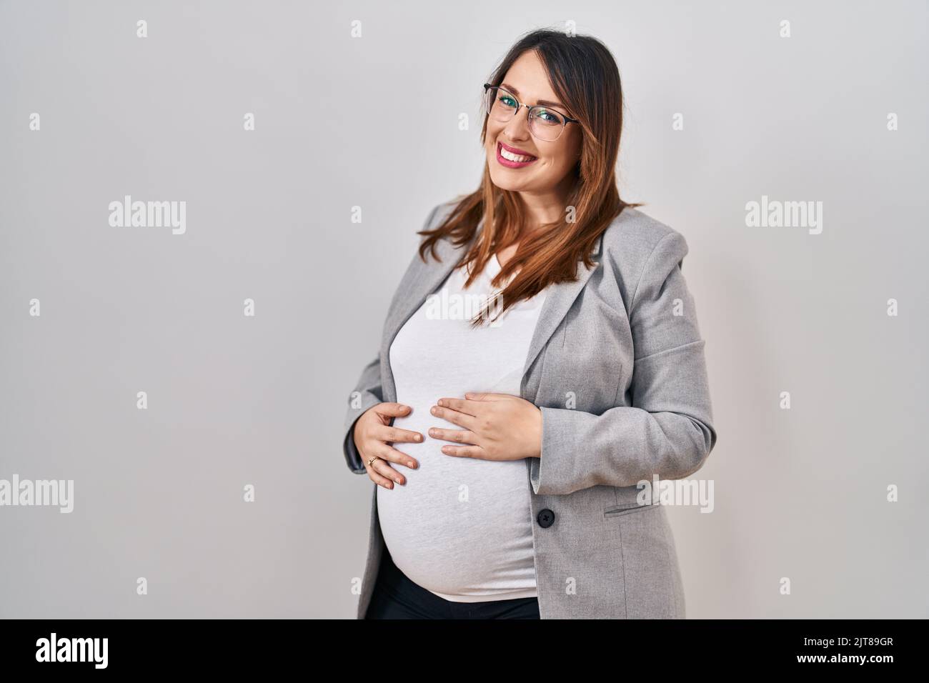 Pregnant business woman standing over white background with serious ...
