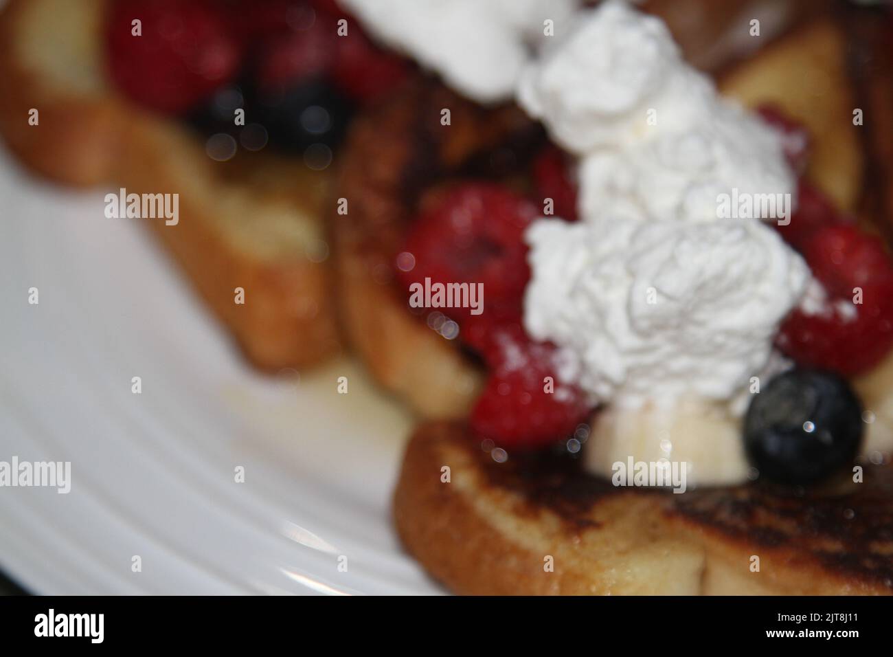 French toast covered with fruit, whipped cream, and syrup on a white plate Stock Photo