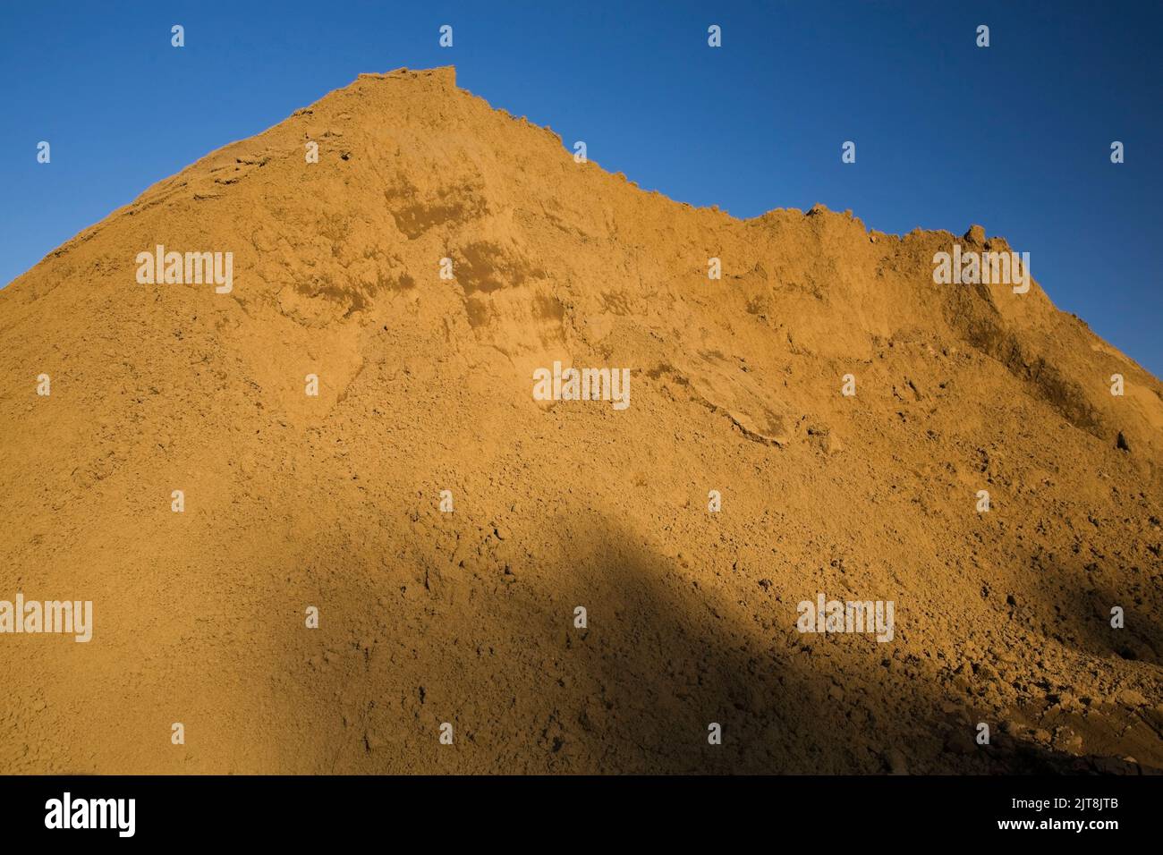 Mound of tan colored sand in a commercial sandpit at sunset. Stock Photo