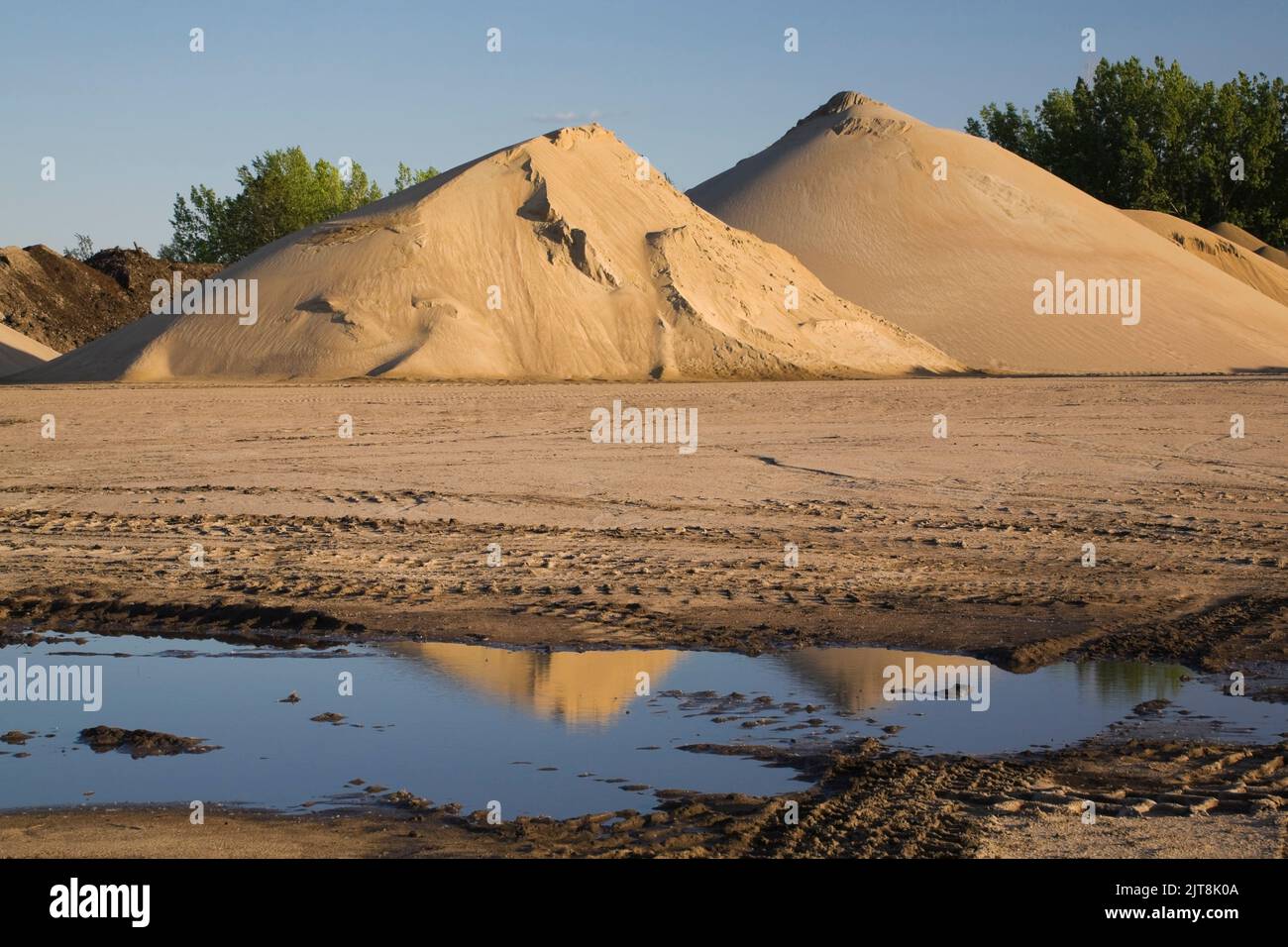 Mounds of tan colored sand and heavy tire tracks in a commercial sandpit after a heavy rainfall. Stock Photo