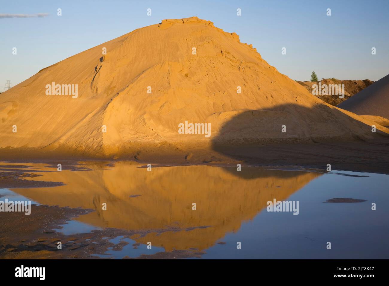 Mounds of golden brown sand in a commercial sandpit after a heavy rainfall. Stock Photo