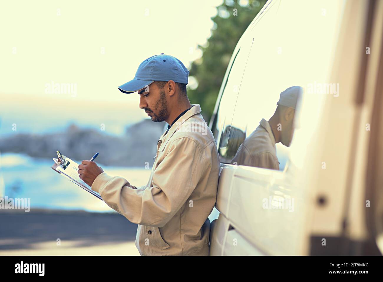 Getting all his logistics down. a delivery man writing on a clipboard