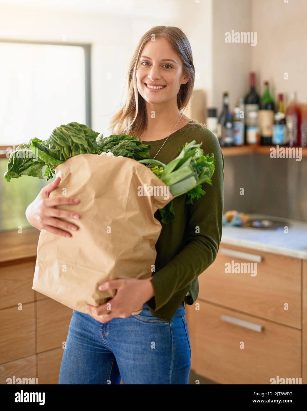 Fresh from the grocers. Portrait of a smiling young woman standing in her kitchen carrying a paper bag full of groceries. Stock Photo