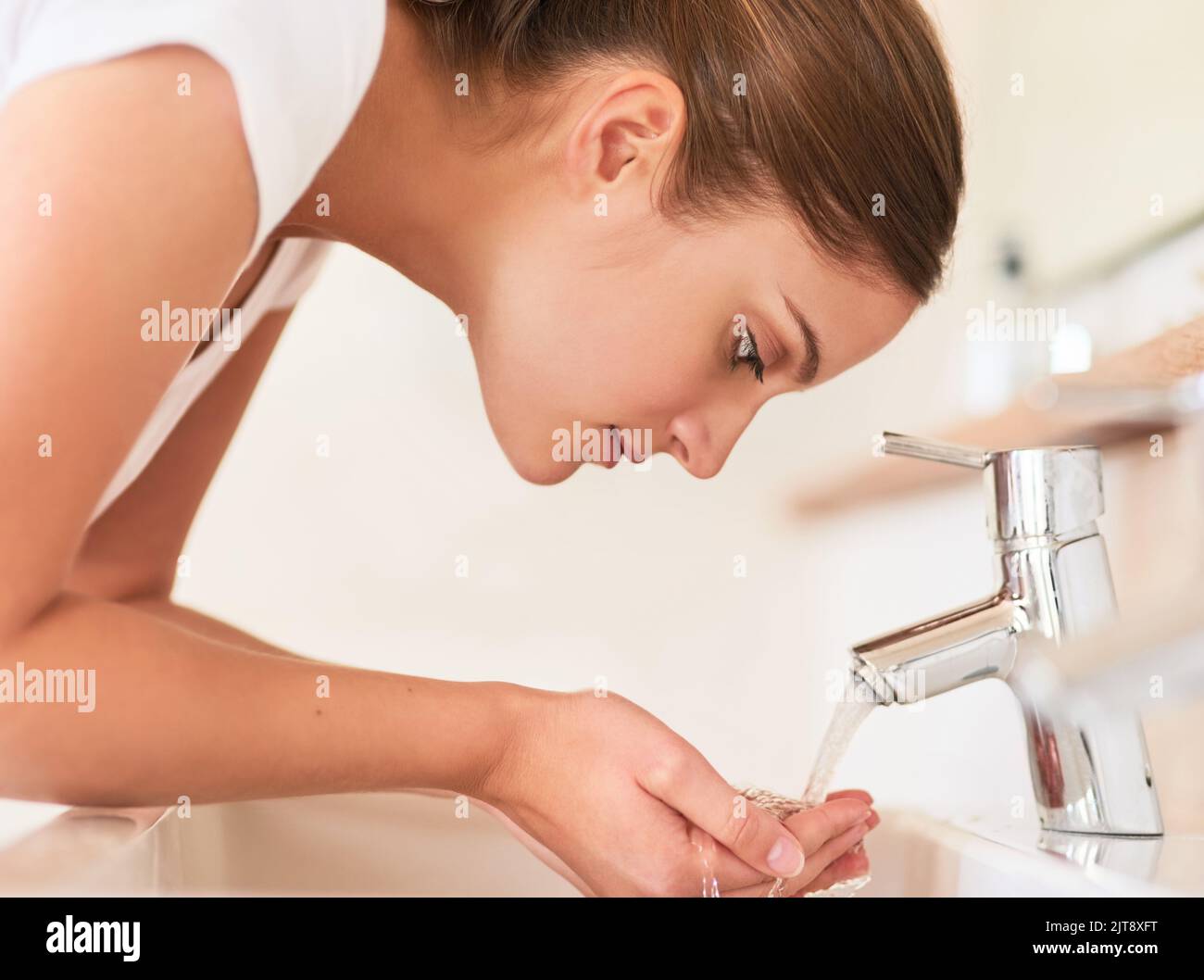 Cleanliness is key. a young woman washing her face in the bathroom. Stock Photo