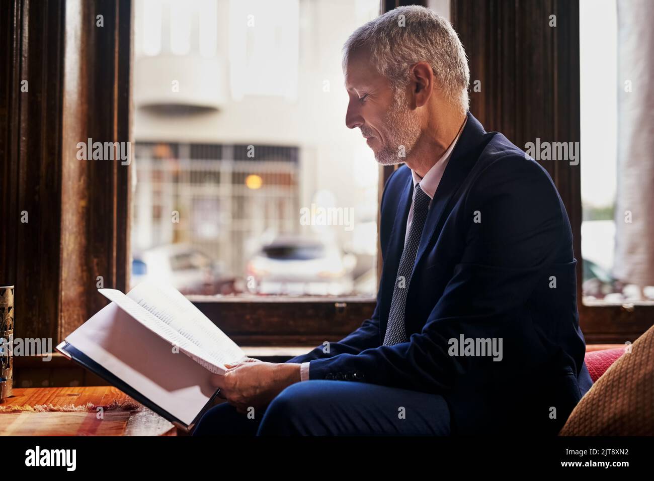 Relaxing at his favorite city spot. a well-dressed mature man reading a menu in a cafe after work. Stock Photo
