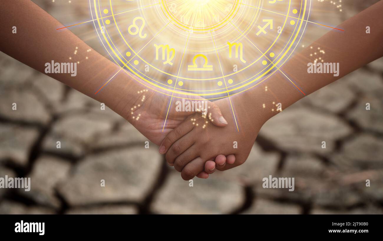 Young boy and girl holding hands in the dried soil with the sun light passing through the hands have astrological symbols. Stock Photo
