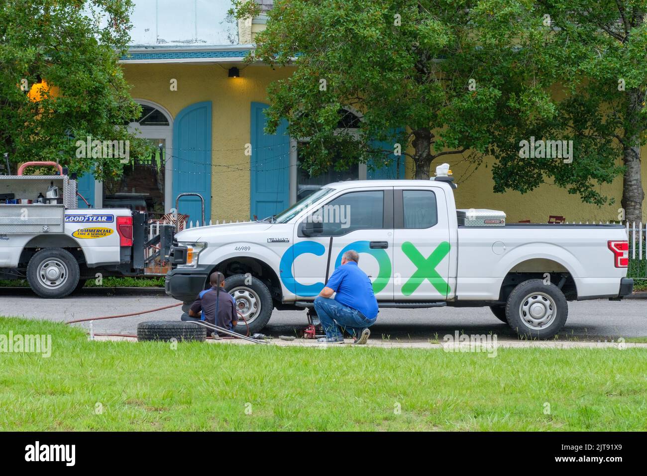 NEW ORLEANS, LA, USA - AUGUST 24, 2022: Repairman from Goodyear Roadside Service changes a tire on a Cox Cable truck as the Cox worker looks on Stock Photo