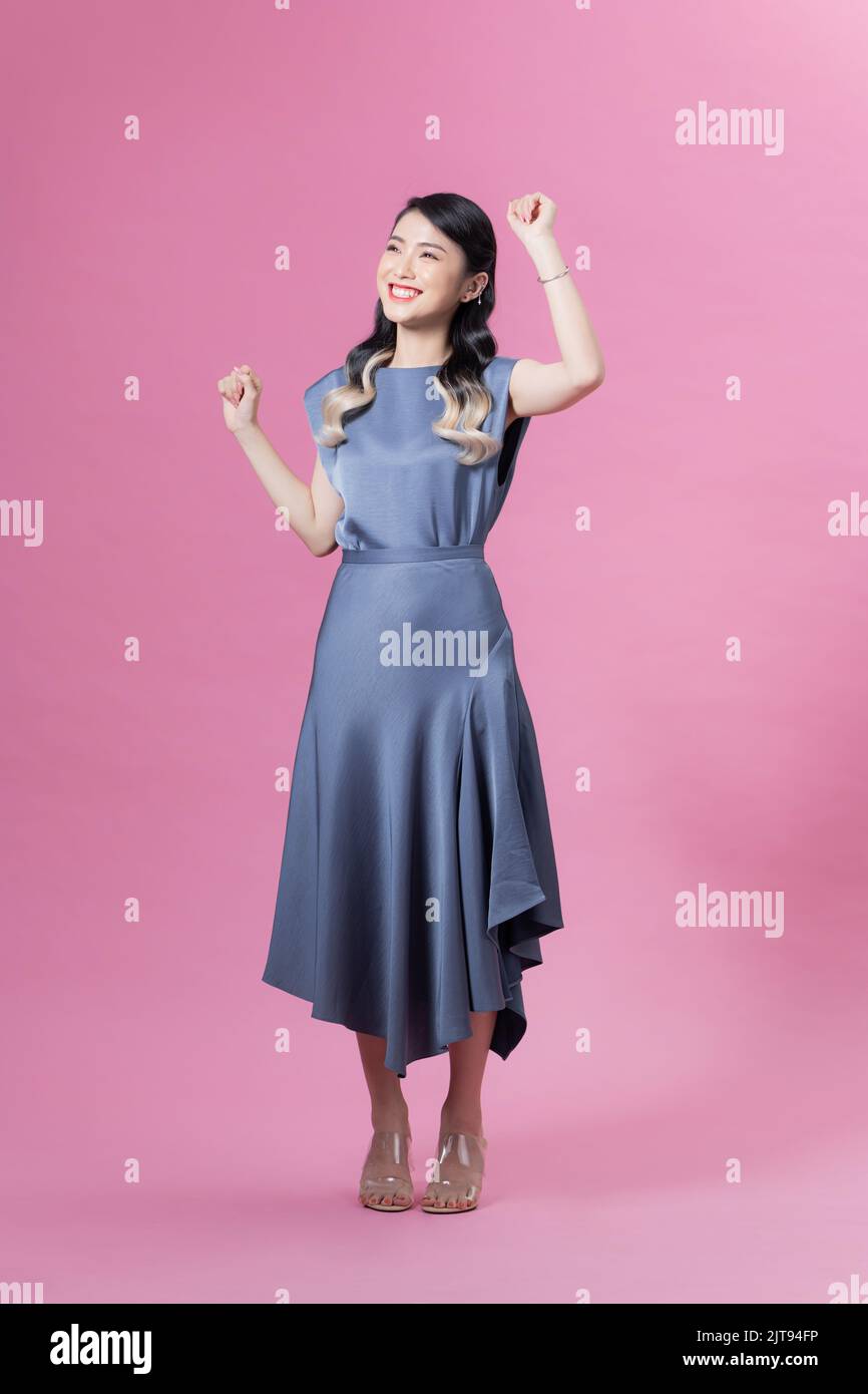 Full length portrait of a pretty young woman wearing blue dress and high heels isolated on a pink background Stock Photo
