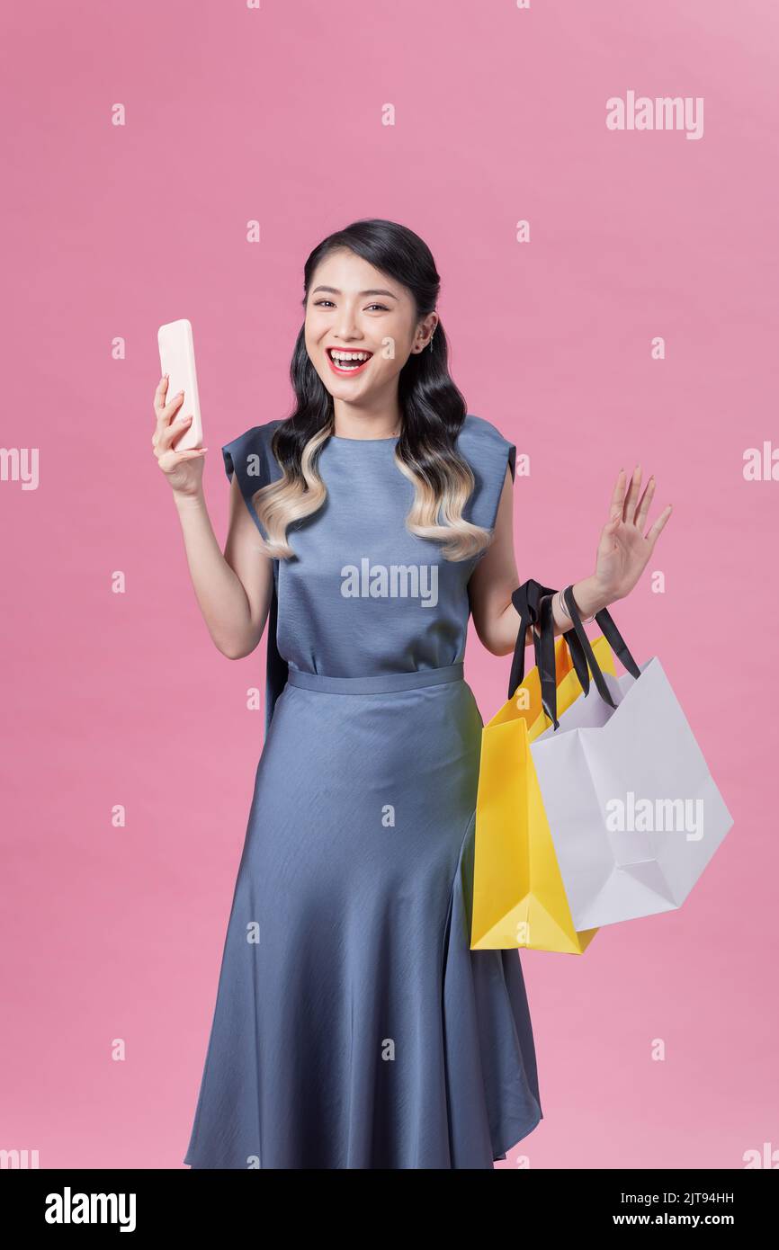 Incredibly excited young woman holding smartphone and shopping bags looking at camera in surprise Stock Photo