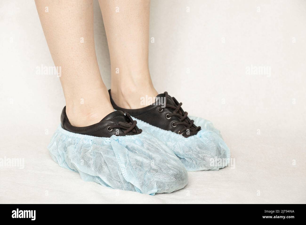 female legs in black shoes and blue disposable boots on a white background, protective shoe covers, shoe covers Stock Photo