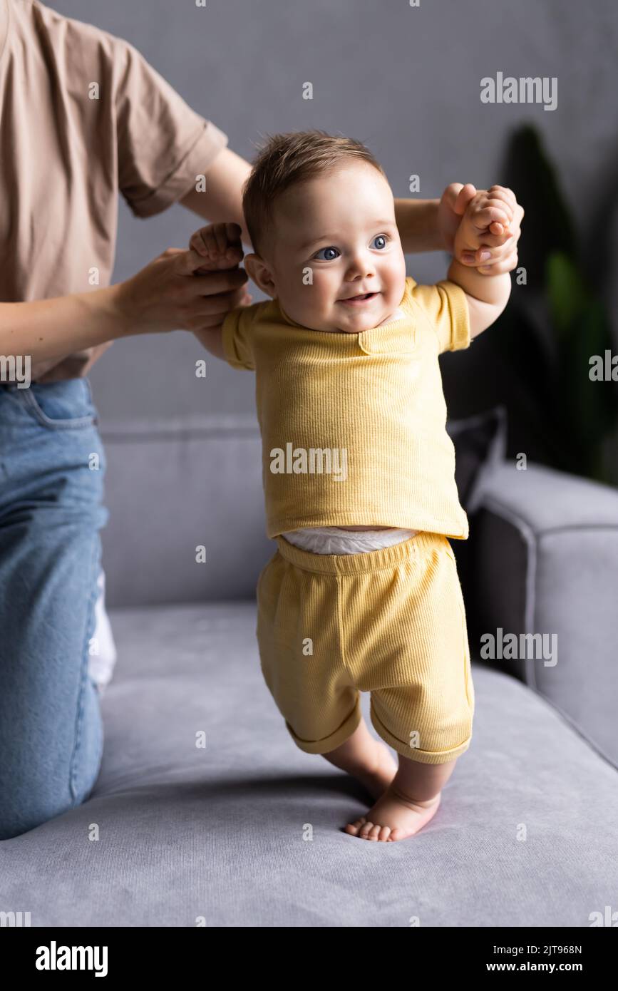 Mother and baby laugh together at home. They are sitting on the sofe in a brightly lit living room at the weekend together, lazy morning, warm and coz Stock Photo