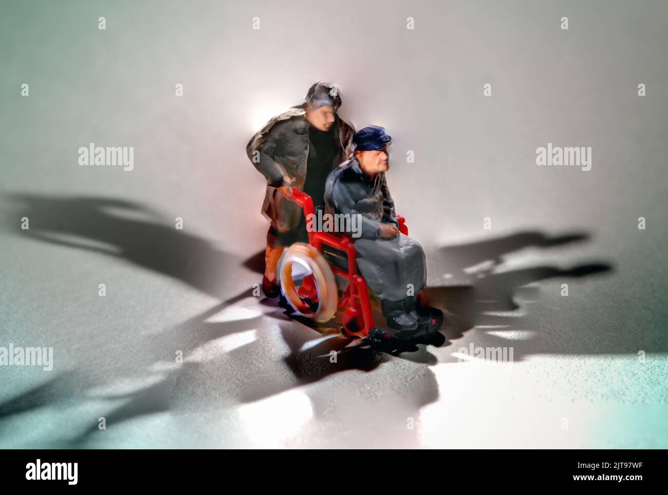 Miniature man pushing a friend or patient in a wheelchair in a concept of disability, mobility, healthcare and recuperation Stock Photo