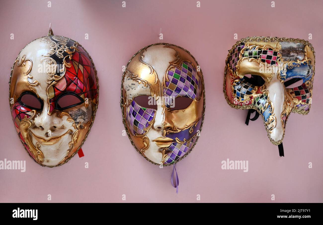 Traditional Venetian masks with colorful geometric ornaments hanging on pink wall during carnival Stock Photo
