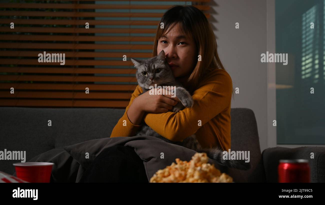 Young asian woman with her lovely cat watching TV at home. Leisure activity, relaxation, hobby concept Stock Photo
