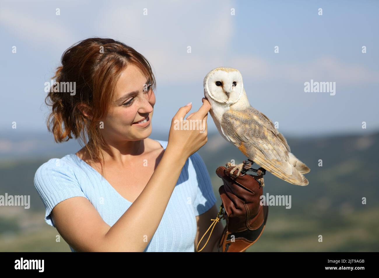 Happy falconer caressing an owl standing in nature Stock Photo
