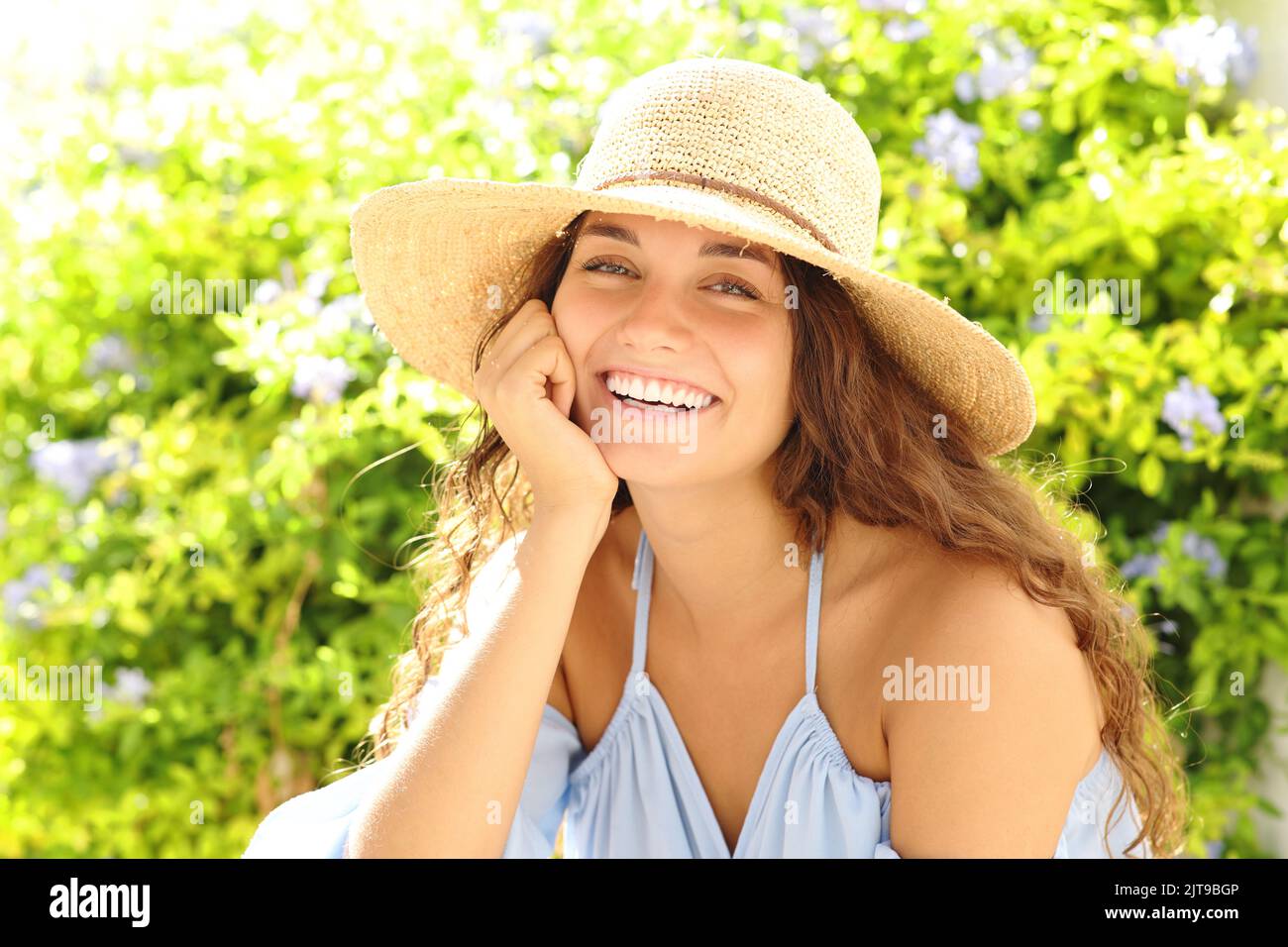 Happy woman with pamela hat smiling at camera in a green garden Stock Photo