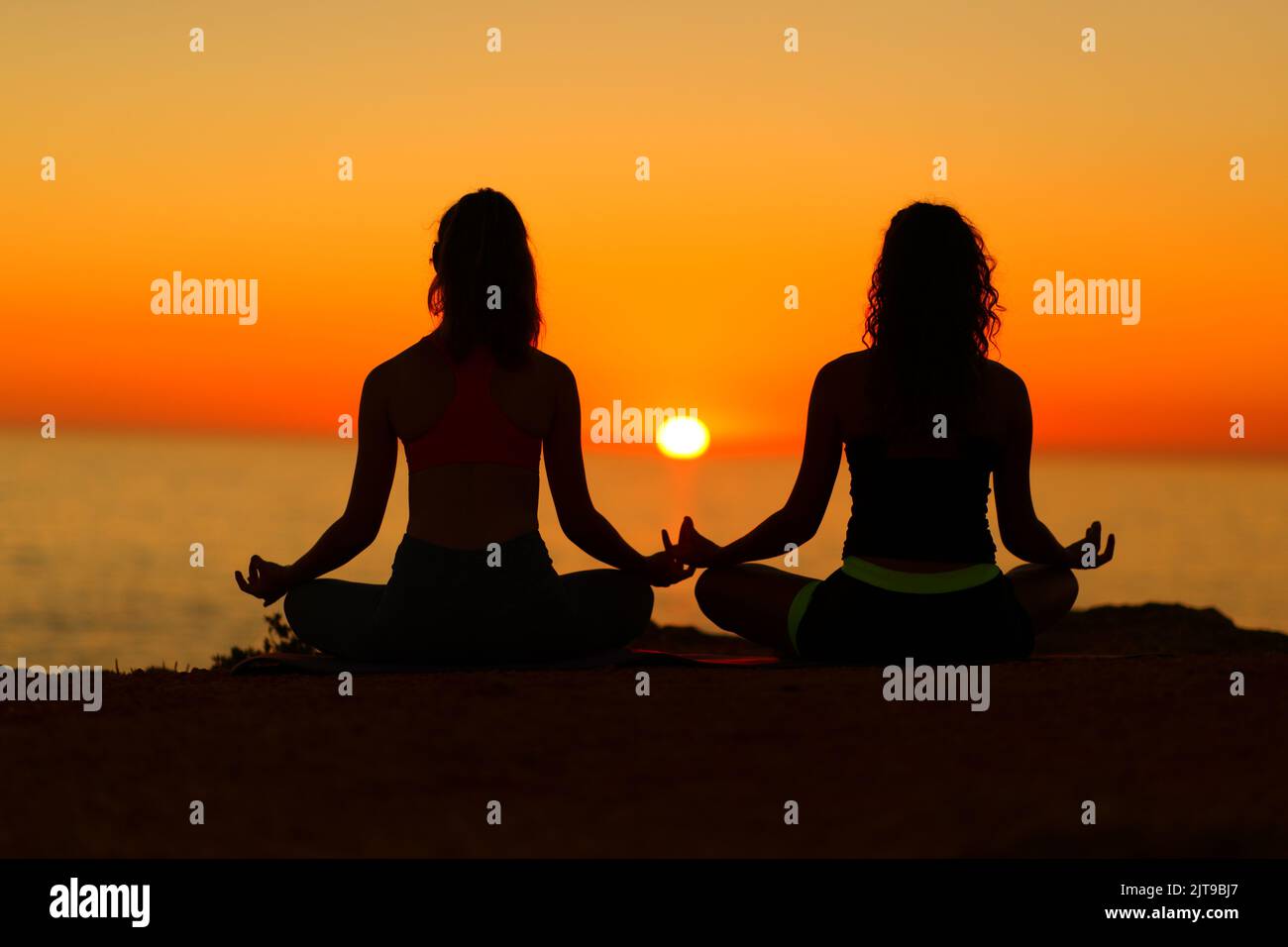 Back view backlight portrait of two women silhouettes doing yoga at sunset on the beach Stock Photo