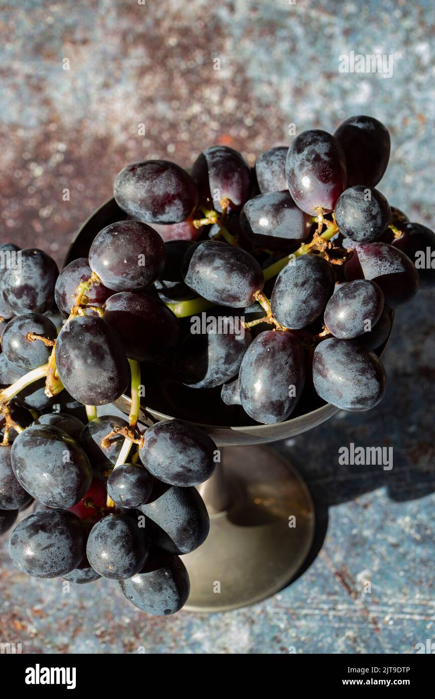 Bunch of black grapes in an old pewter goblet. On a grunge background
