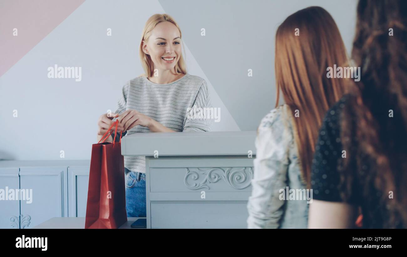 Friendly female cashier is taking garment from customer standing in