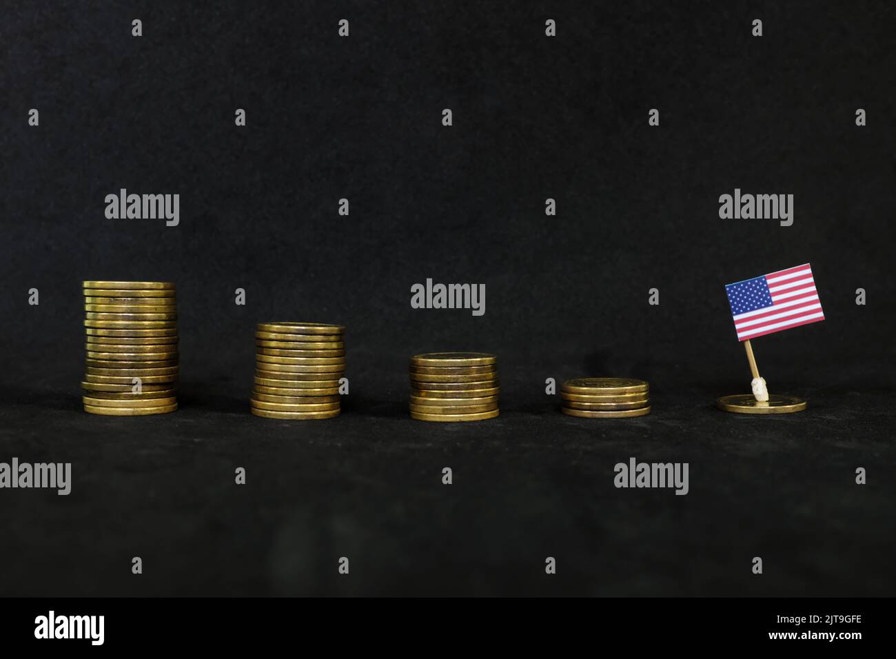 US economic recession, financial crisis and dollar depreciation concept. Flag of America in decreasing stack of coins in dark black background. Stock Photo