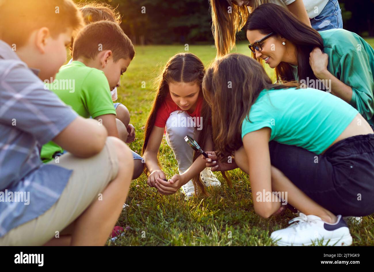 Group of school students learn about environment and study insects in green grass Stock Photo