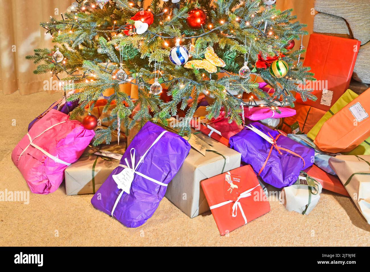 Eco friendly colourful recyclable wrapping paper for Christmas gift & present wrap placed at base of decorated artificial Xmas tree with LED lights UK Stock Photo
