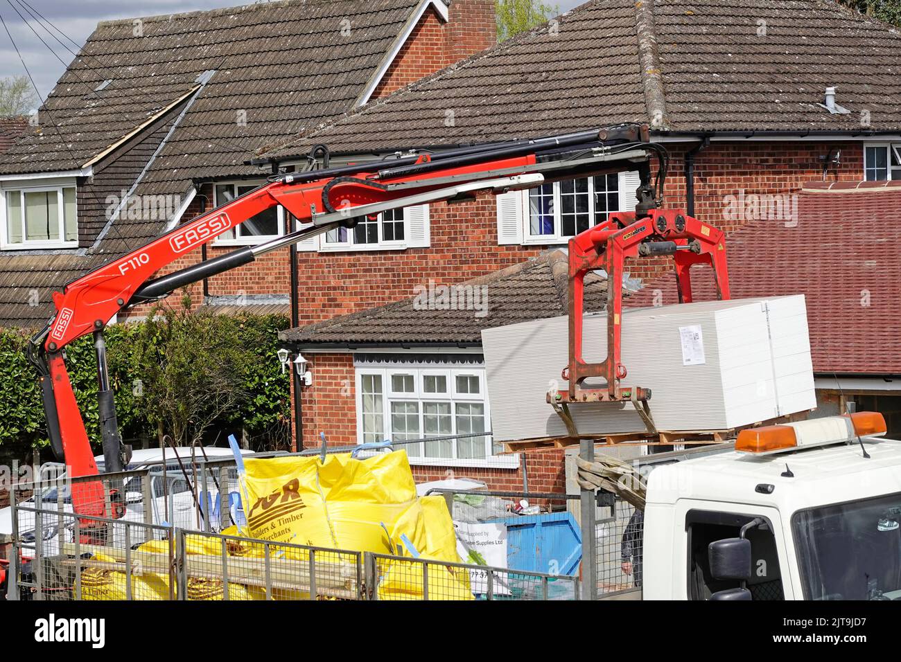 Close up builders merchant lorry truck mounted hydraulic crane delivery driver below controls building construction site materials offload  England UK Stock Photo
