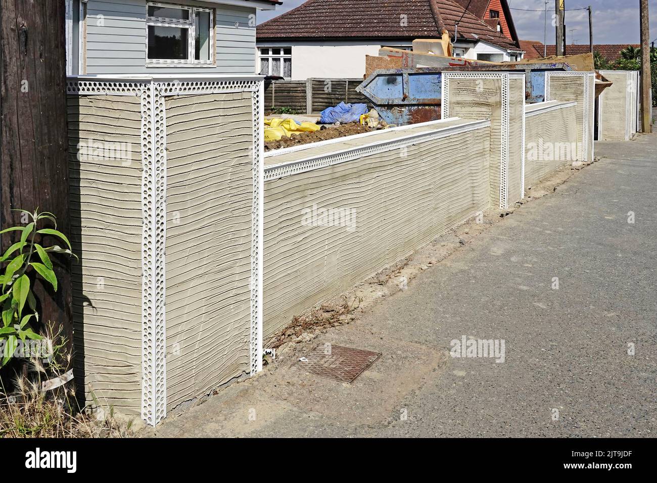 Concrete block front boundary wall & piers at new build bungalow home white plastic angle beads nailed onto render scratch coat abutting pavement UK Stock Photo