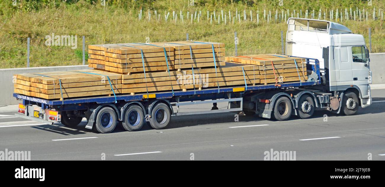 Side view of hgv lorry truck haulage business with articulated flat bed articulated trailer load of bundled construction timber driving on motorway UK Stock Photo