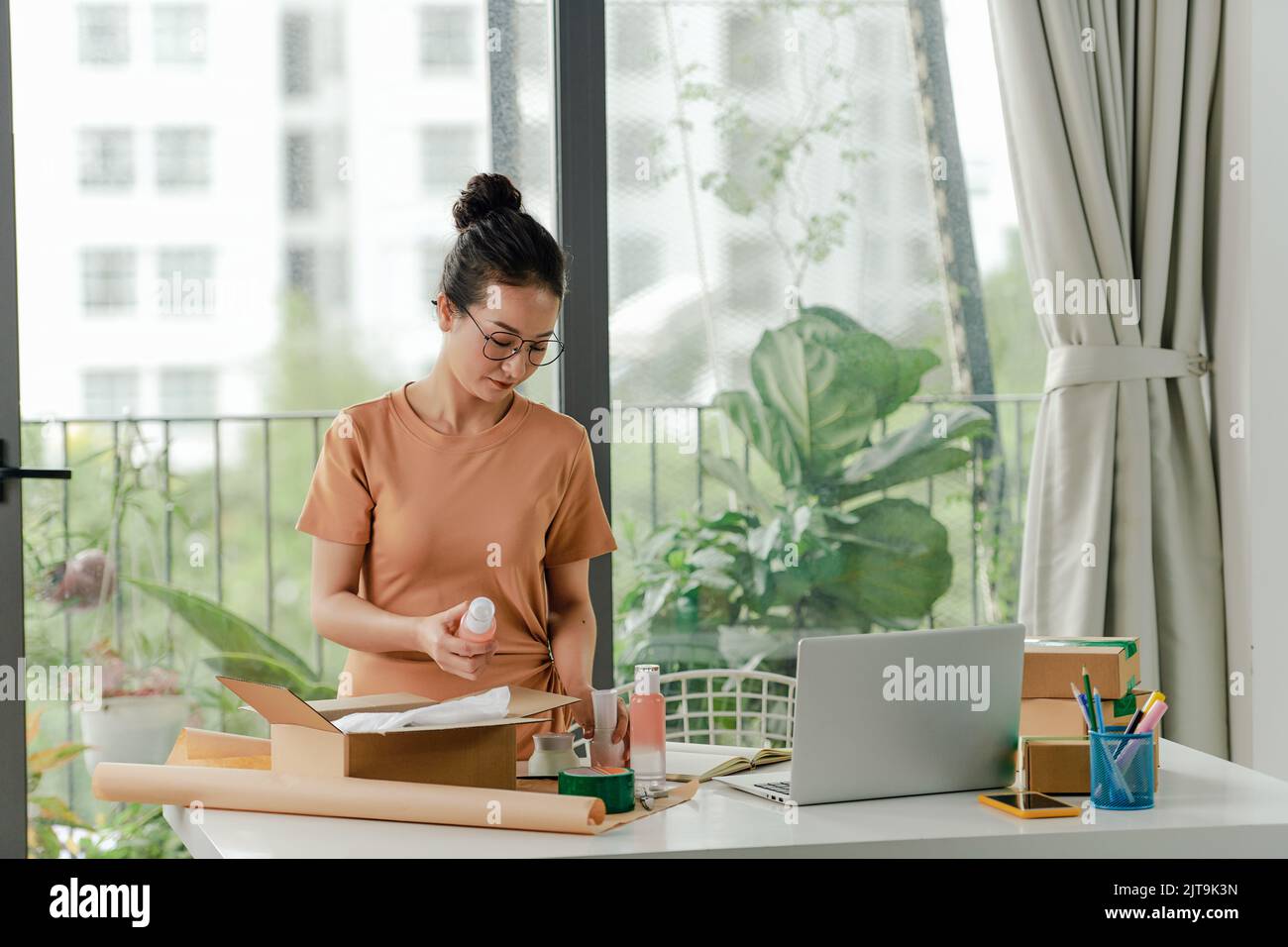 Woman packing cosmetic products in box for courier or poster shipment. Stock Photo