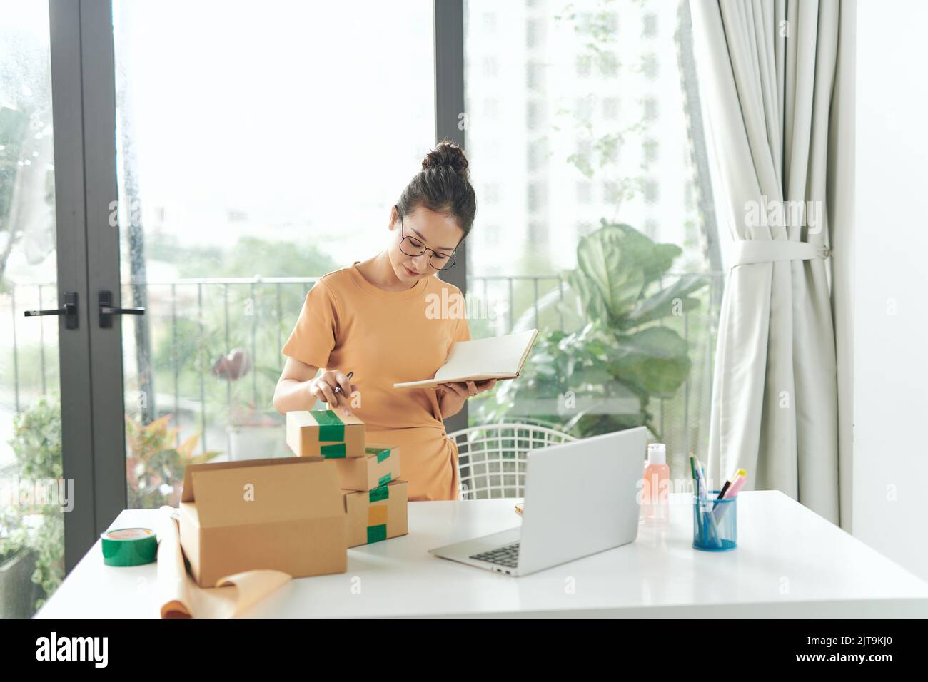 woman checking purchase order in laptop and write in the delivery on package box sell online Stock Photo
