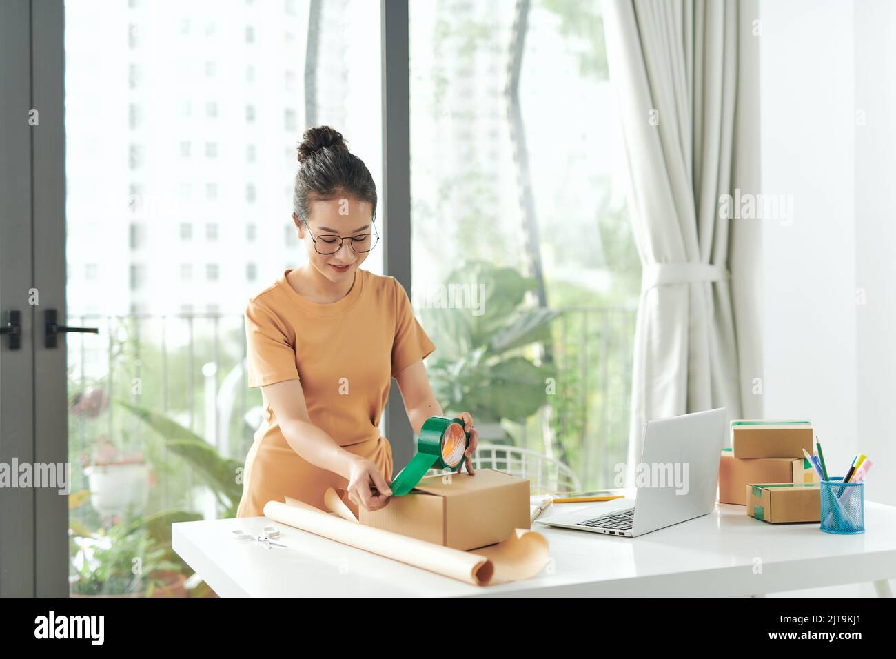 Startup small business owner working at home, women sealing cardboard box with adhesive tape, Stock Photo