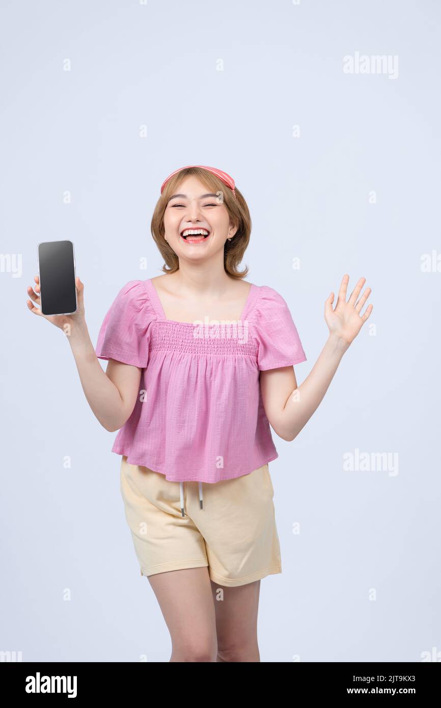 Happy smiling asian girl in pajamas and sleeping mask tracking her sleep with mobile app, showing smartphone screen and look pleased, white background Stock Photo
