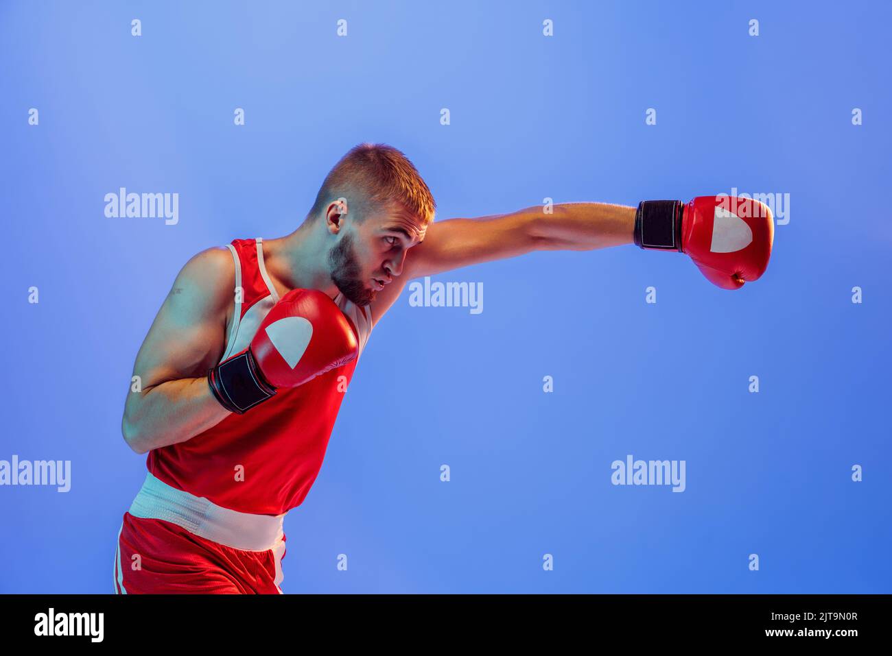 Knockout punch. Male boxer in red uniform and boxing gloves training