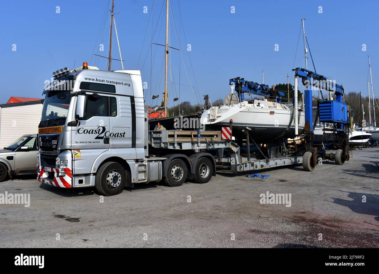Sailing boat being transported on a truck into East Llanion boatyard, East Llanion, Pembrokeshire, Wales Stock Photo