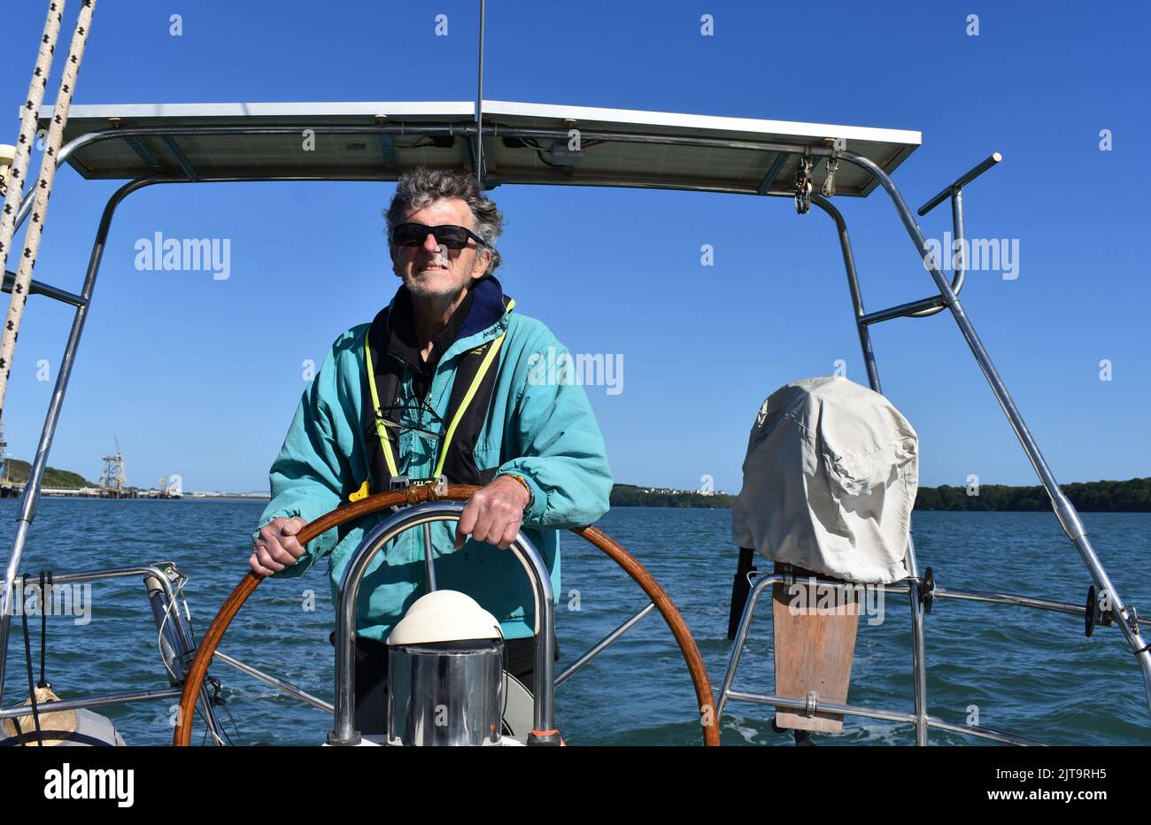 Skipper steering a yacht down the Milford Haven waterway, Pembrokeshire, Wales Stock Photo