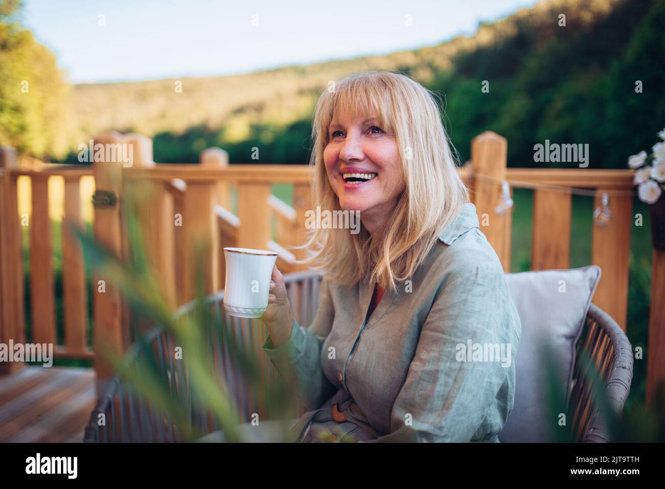 Happy mature woman relaxing with morning coffee on terrace in summer ...