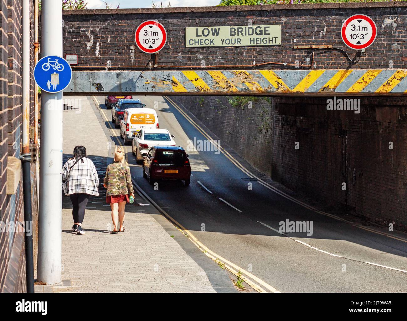 People walking and cars passing under a signed low bridge. An urban scene Stoke-on-Trent, UK Stock Photo