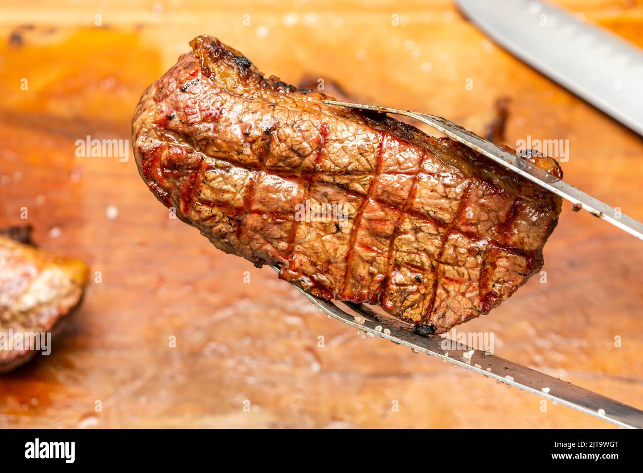 a barbecue tong holding grilled tritip steak on a barbecue party Stock