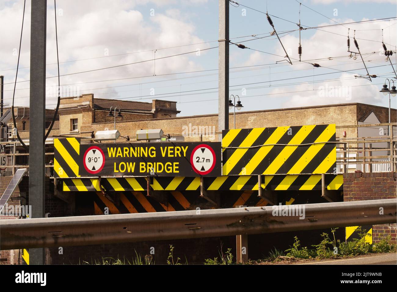 Image of the very low road bridge, 2.7m, next to Ely railway station, Ely Cambridgeshire with an armco crash barrier and electric train wires Stock Photo