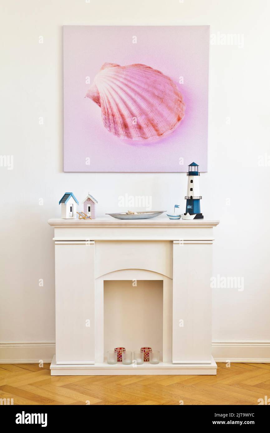 Interior shot of a square canvas print of a pink shell picture and a faux fireplace, against the white wall of an old building with parquet flooring. Stock Photo